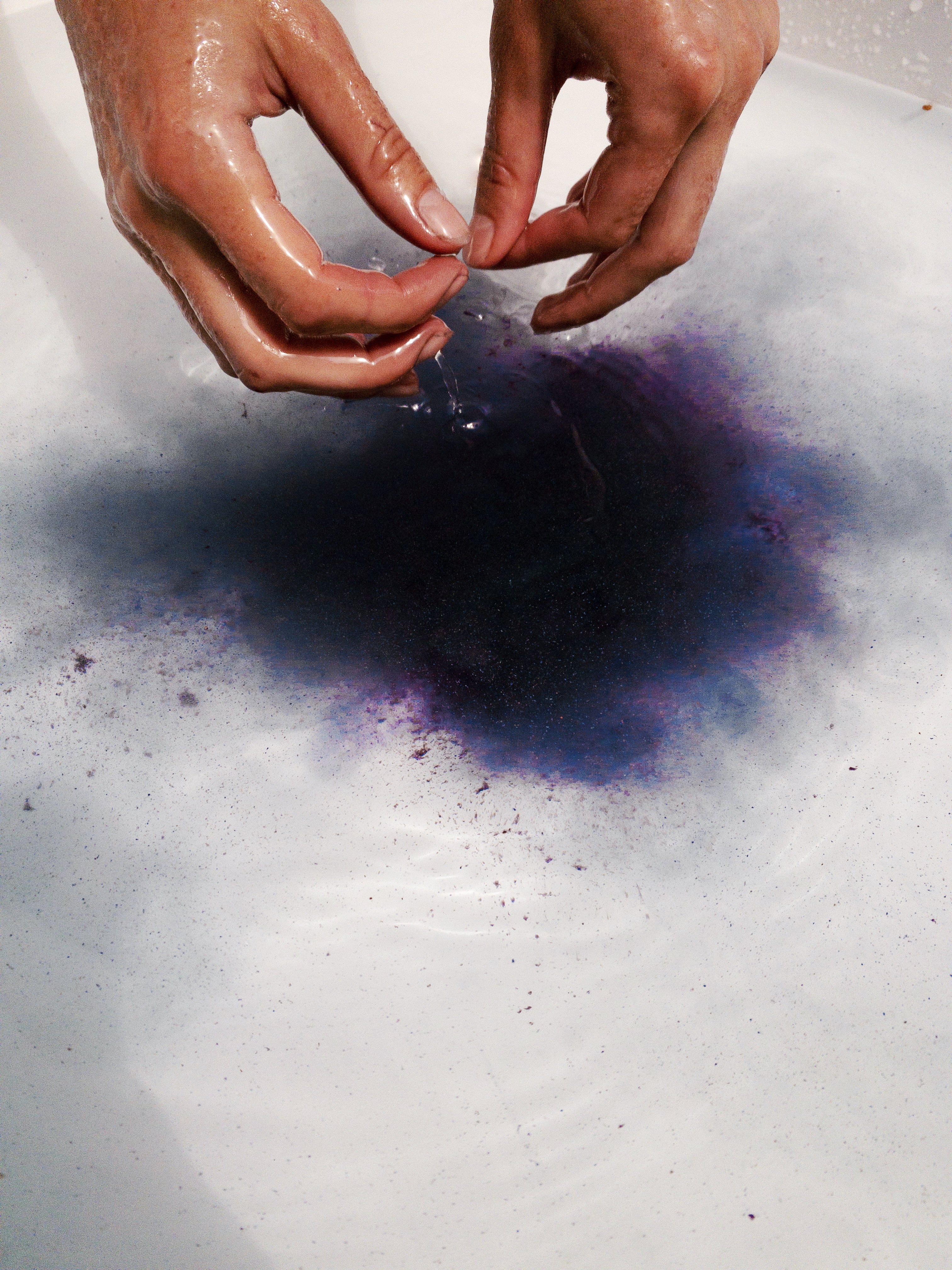 A person dissolving Heathen's purple herbal bath soak into bath water. 