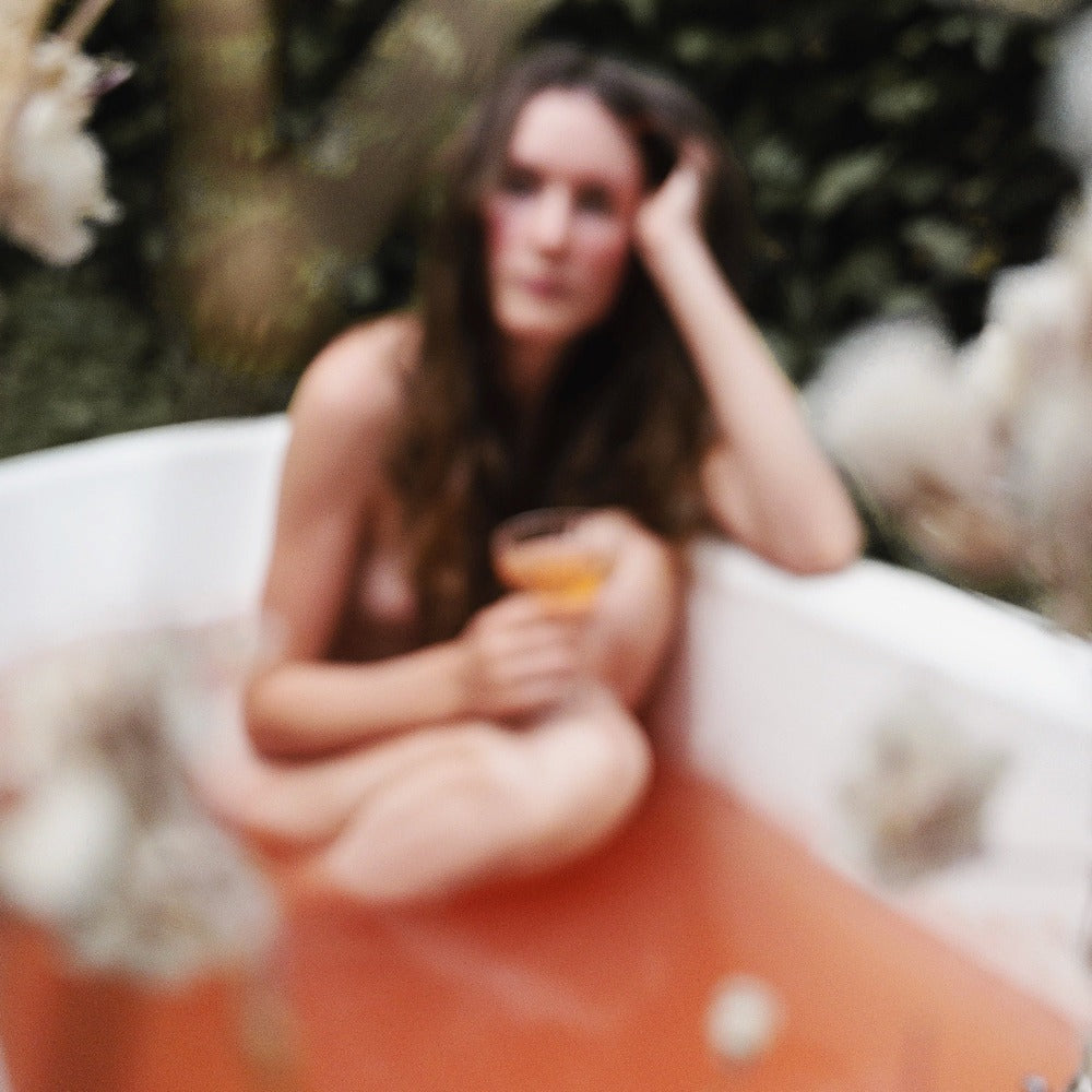 Image of a woman bathing in a Forgotten Fruit pink herbal bath soak. 